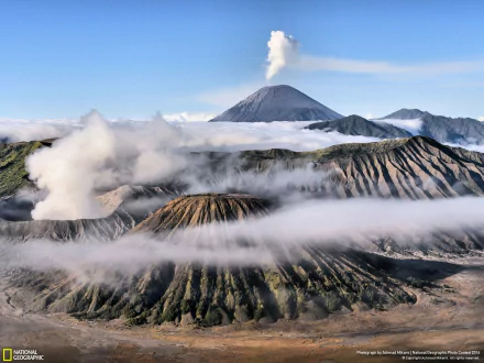 Stunning HD wallpaper of Mount Bromo, featuring its dramatic volcanic landscape with steam rising amidst clouds, capturing the beauty of nature.