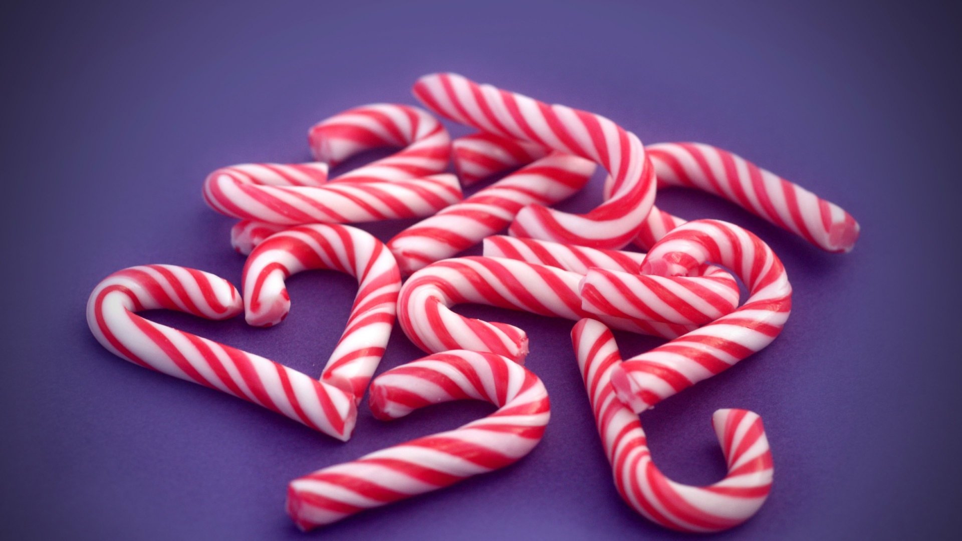 A colorful arrangement of pink and white candy canes, some shaped like hearts, set against a vibrant purple background, adding an artistic touch of love. 4K Ultra HD wallpaper.