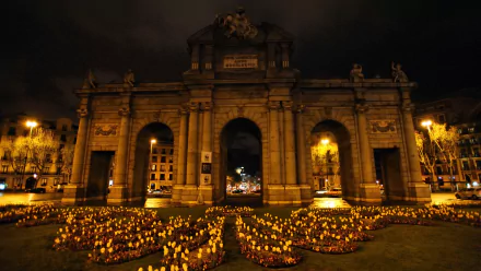 HD PC desktop wallpaper and background: illuminated Puerta de Alcalá at night — a man-made stone archway framed by flowerbeds and warm streetlights.
