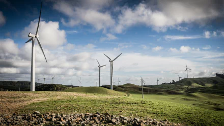 A scenic view of wind turbines on rolling green hills under a dynamic sky, captured as a high-definition desktop wallpaper background showcasing sustainable energy.