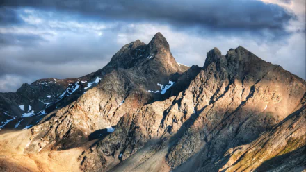 Majestic alpine peaks rise dramatically under a cloudy sky, showcasing the stunning beauty of nature in the Alps. This HD wallpaper captures their rugged terrain and vibrant light.