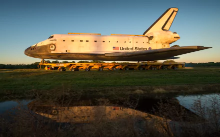 HD desktop wallpaper of the Space Shuttle Discovery vehicle resting on a transport platform with a clear sky and grass field in the background.