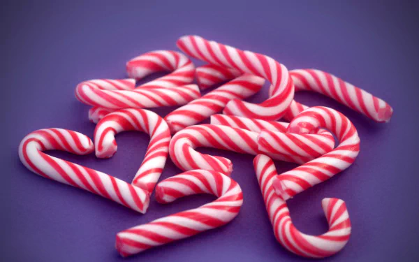 A colorful arrangement of pink and white candy canes, some shaped like hearts, set against a vibrant purple background, adding an artistic touch of love. 4K Ultra HD wallpaper.
