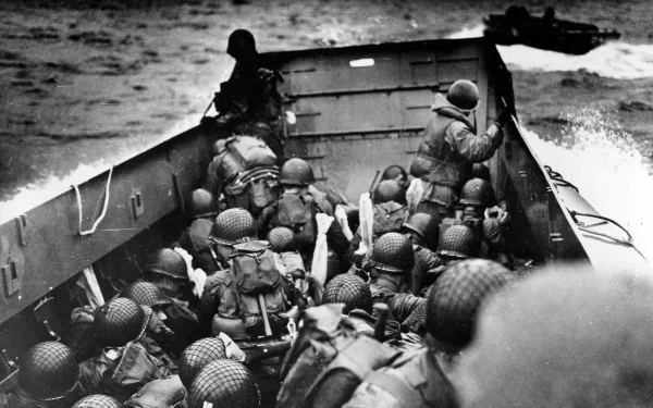 Black and white HD desktop wallpaper depicting armed soldiers in a landing craft approaching the shore during the D-Day military invasion.