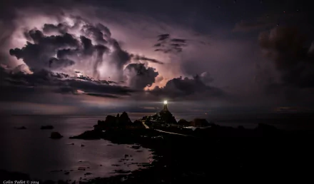 A dramatic sunset casts vibrant colors over a tranquil sea, where a lighthouse stands against a backdrop of swirling clouds, creating a stunning HD desktop wallpaper.