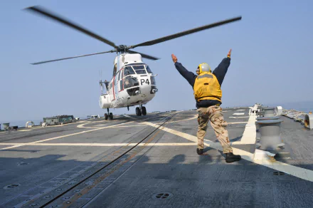 A Marine guides an Aérospatiale SA 330 Puma helicopter landing on the deck of the USS Preble navy ship.