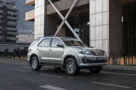 A high-definition desktop wallpaper featuring a silver Toyota Fortuner SUV parked in an urban setting with modern architecture in the background.
