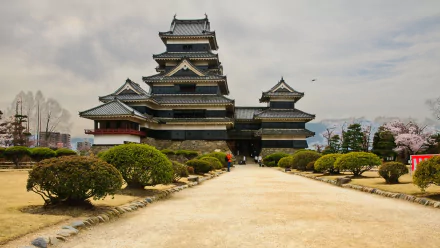 HD PC desktop wallpaper and background of man-made Matsumoto Castle framed by gardens and a gravel path under a cloudy sky.