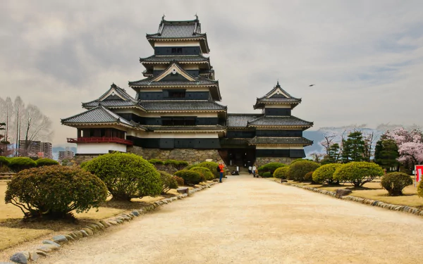 HD PC desktop wallpaper and background of man-made Matsumoto Castle framed by gardens and a gravel path under a cloudy sky.