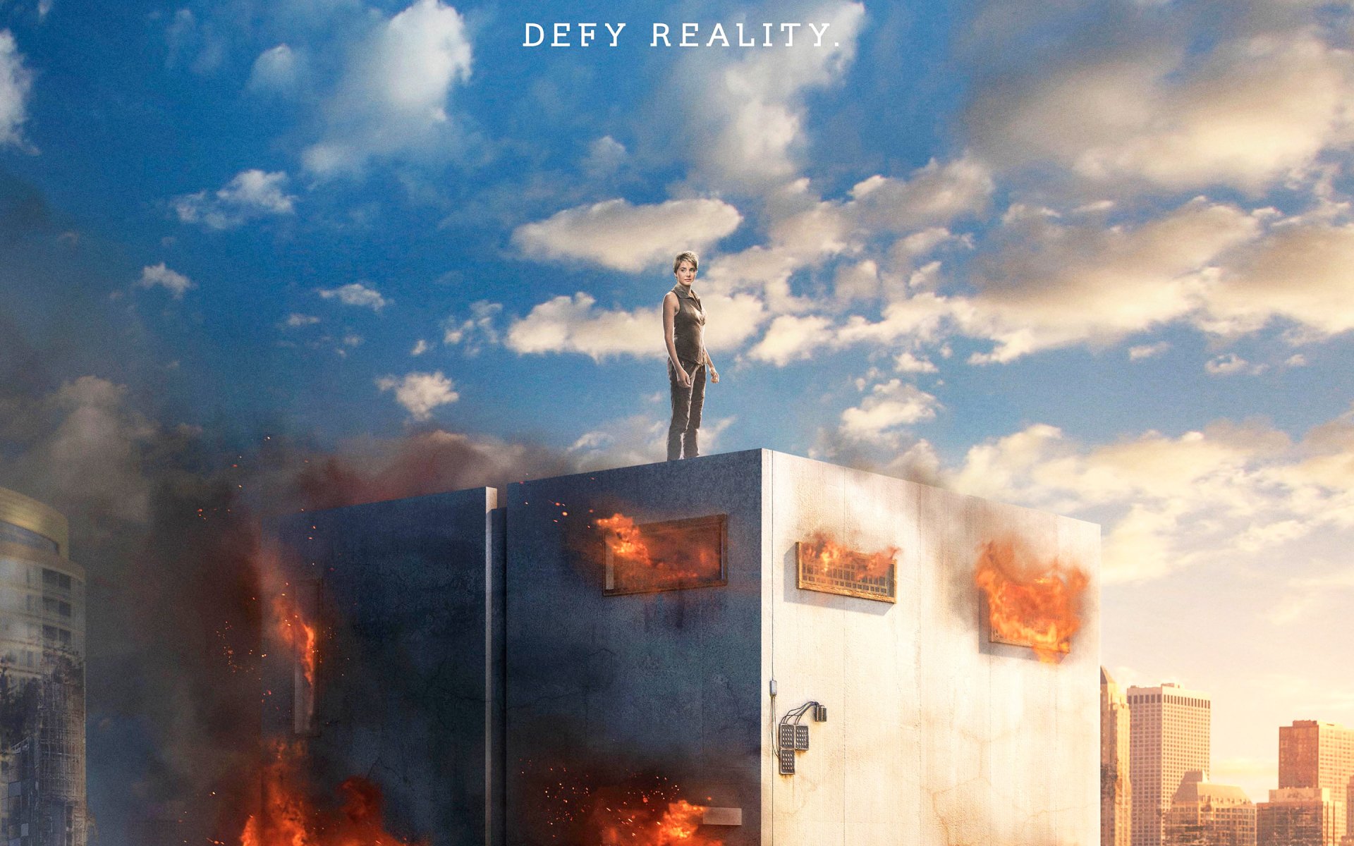 HD PC desktop wallpaper featuring a dramatic scene from the movie Insurgent with a character standing atop a burning structure under a cloudy sky and the text DEFY REALITY.