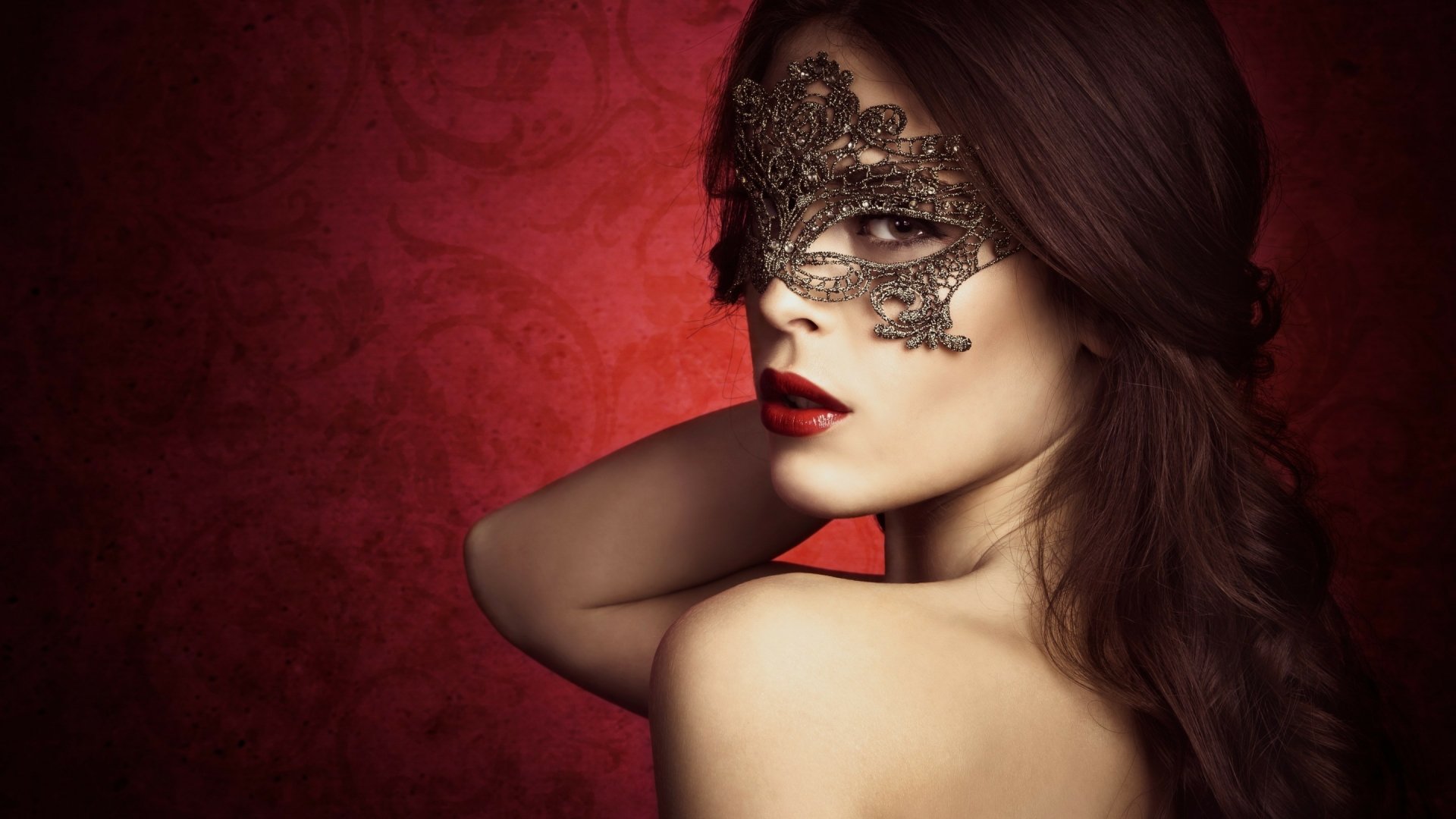 HD desktop wallpaper featuring a close-up portrait of a model wearing an ornate black lace mask against a rich red background, highlighting elegant photography.