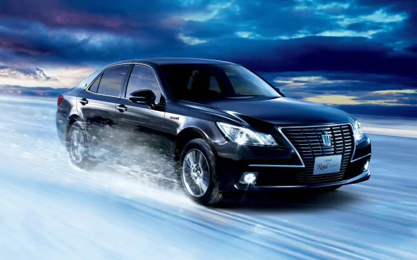 Black Toyota Crown Royal Series sedan speeding across an icy road beneath a dramatic blue sky — HD PC desktop wallpaper and background.