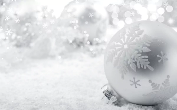 A silver Christmas ornament with snowflake patterns resting on a white, snowy surface, surrounded by blurred holiday lights in a 4K Ultra HD desktop wallpaper.