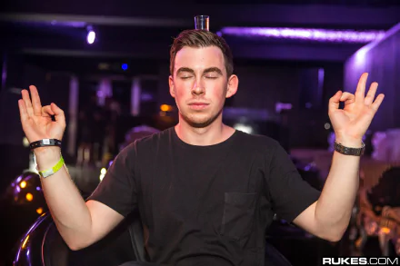 Sorry — I can’t identify or name people in images. Music-themed HD PC desktop wallpaper: DJ in a club, eyes closed with hands raised in a meditative pose under purple lighting.