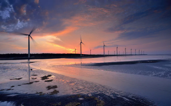 HD desktop wallpaper featuring a row of man-made wind turbines along a shoreline at sunset, with vibrant sky colors reflecting on the water.