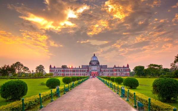 A stunning view of Cooch Behar Palace at sunset, with vibrant skies and lush greenery framing the grand structure, making it an impressive backdrop for desktop wallpaper.