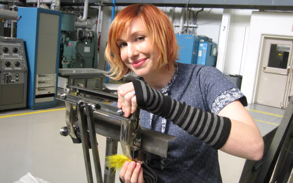 HD PC desktop wallpaper and background: MythBusters TV show workshop scene — red-haired woman smiles while adjusting a metal rig in a lab-like garage.