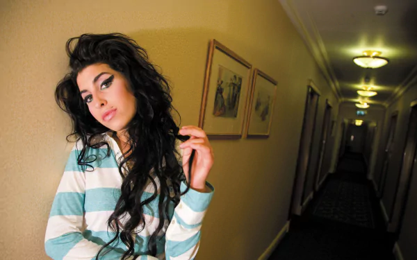 2K Quad HD PC wallpaper — moody portrait of an unnamed English singer with beehive-style hair and winged eyeliner, striped top, leaning in a dim hotel corridor, music-themed desktop background.