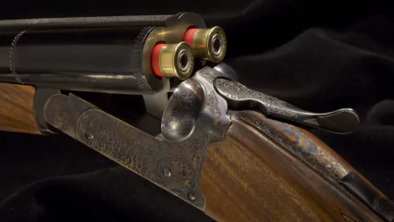 Close-up HD desktop wallpaper of a man-made shotgun, showcasing detailed engraving and two red shotgun shells loaded in the open barrel.