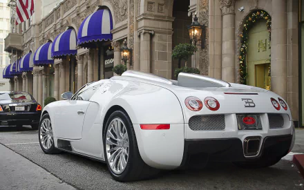 A sleek white Bugatti parked on a city street in front of a historic building with blue awnings, captured in HD for a PC desktop wallpaper.