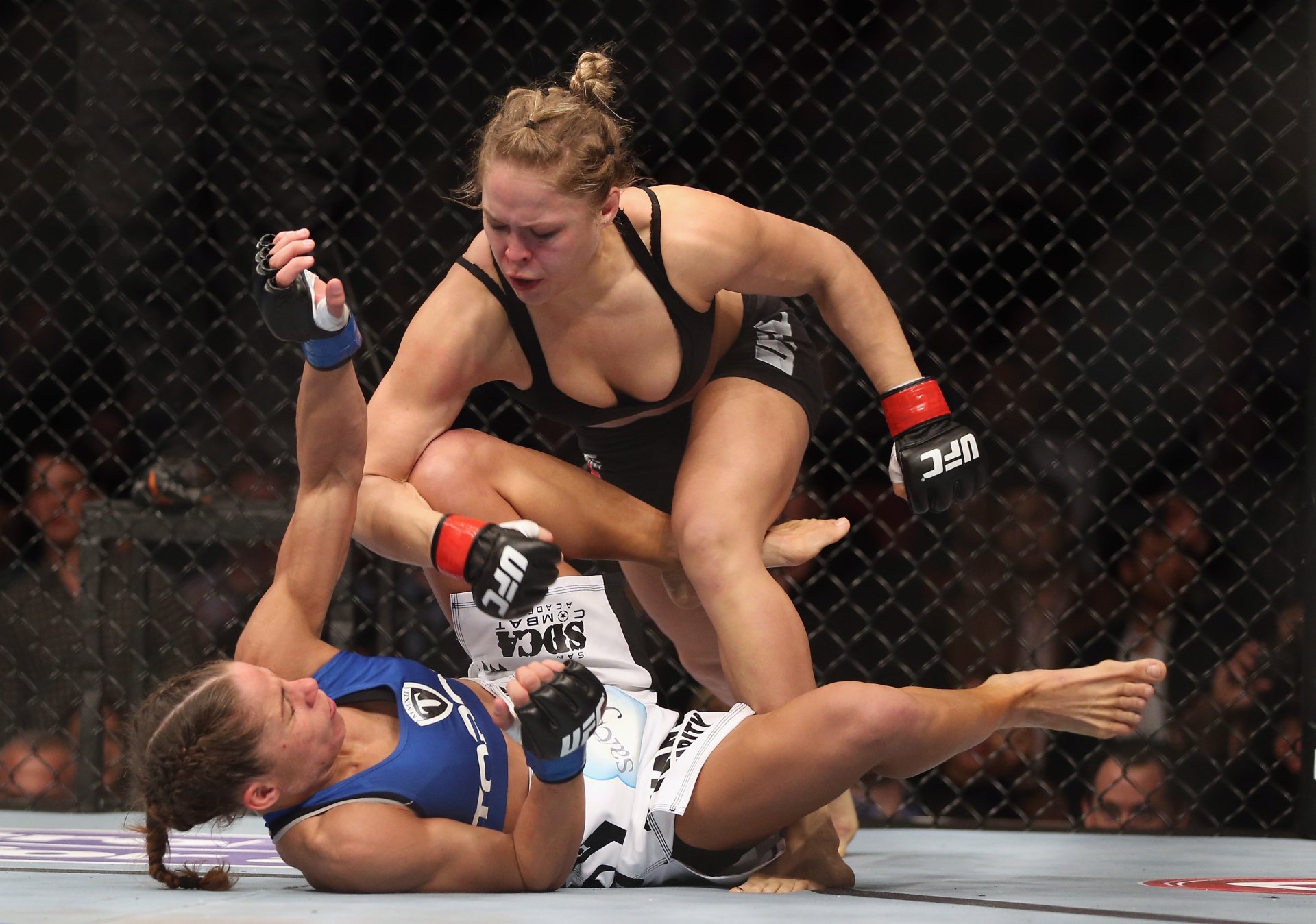 HD sports wallpaper featuring Ronda Rousey in action during a UFC fight inside the octagon, showcasing intense mixed martial arts competition.