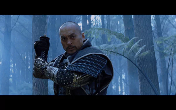 A character from the movie The Last Samurai, dressed in traditional armor, stands poised with a sword in a misty forest, showcasing the film's dramatic atmosphere. HD desktop wallpaper.