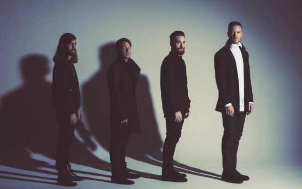 A striking HD wallpaper featuring the American alternative band Imagine Dragons, showcasing the members standing in a line against a softly lit background.