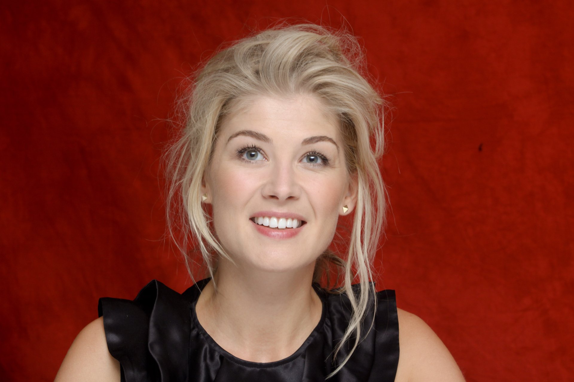 HD desktop wallpaper of Rosamund Pike smiling in front of a red background.
