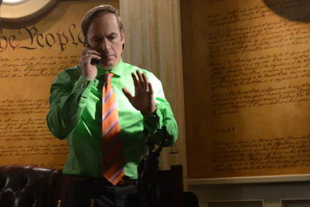 HD wallpaper of a character from Breaking Bad, portrayed by actor Bob Odenkirk, talking on the phone in an office with script-covered walls.