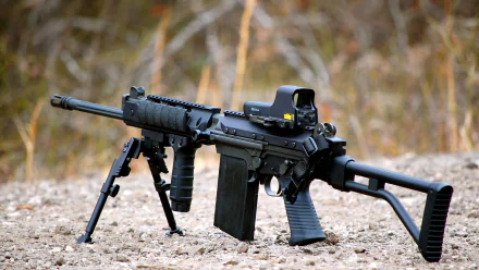 HD desktop wallpaper featuring a man-made FN FAL rifle resting on the ground with a blurred natural background.
