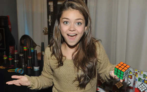 HD wallpaper featuring a cheerful young person from Modern Family, holding a Rubik's Cube with a surprise expression.