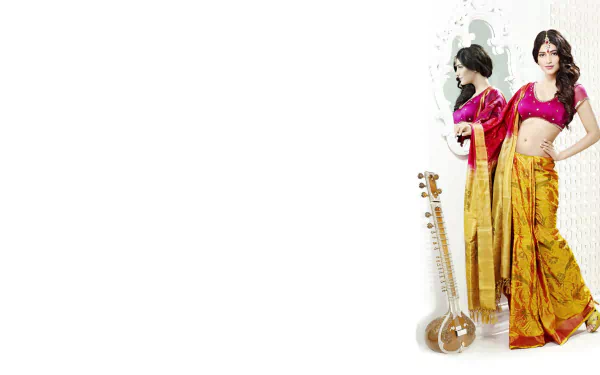 A captivating HD wallpaper featuring Bollywood celebrity Shruti Haasan in a beautiful saree, posing elegantly in front of a mirror with a traditional musical instrument beside her.