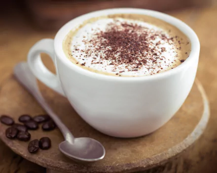 A close-up of a cappuccino topped with cocoa powder in a white cup, accompanied by coffee beans, set against a warm background. 4K Ultra HD quality for a stunning desktop wallpaper.
