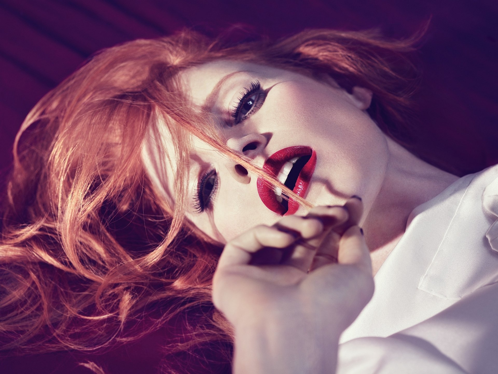 HD PC desktop wallpaper of a red-haired celebrity in a close-up pose — bold red lipstick, dramatic eye makeup, hand near mouth, reclining on a dark background.
