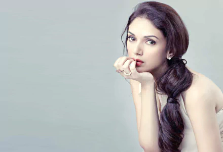 HD desktop wallpaper featuring celebrity Aditi Rao Hydari, with a soft background and the actress posing thoughtfully with her hand near her mouth, showcasing her elegant and serene expression.