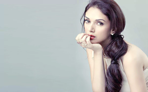 HD desktop wallpaper featuring celebrity Aditi Rao Hydari, with a soft background and the actress posing thoughtfully with her hand near her mouth, showcasing her elegant and serene expression.