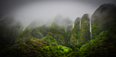 Lush green mountains shrouded in mist, featuring cascading waterfalls amidst the tropical jungle of Oahu, Hawaii. A stunning 4K Ultra HD nature wallpaper.