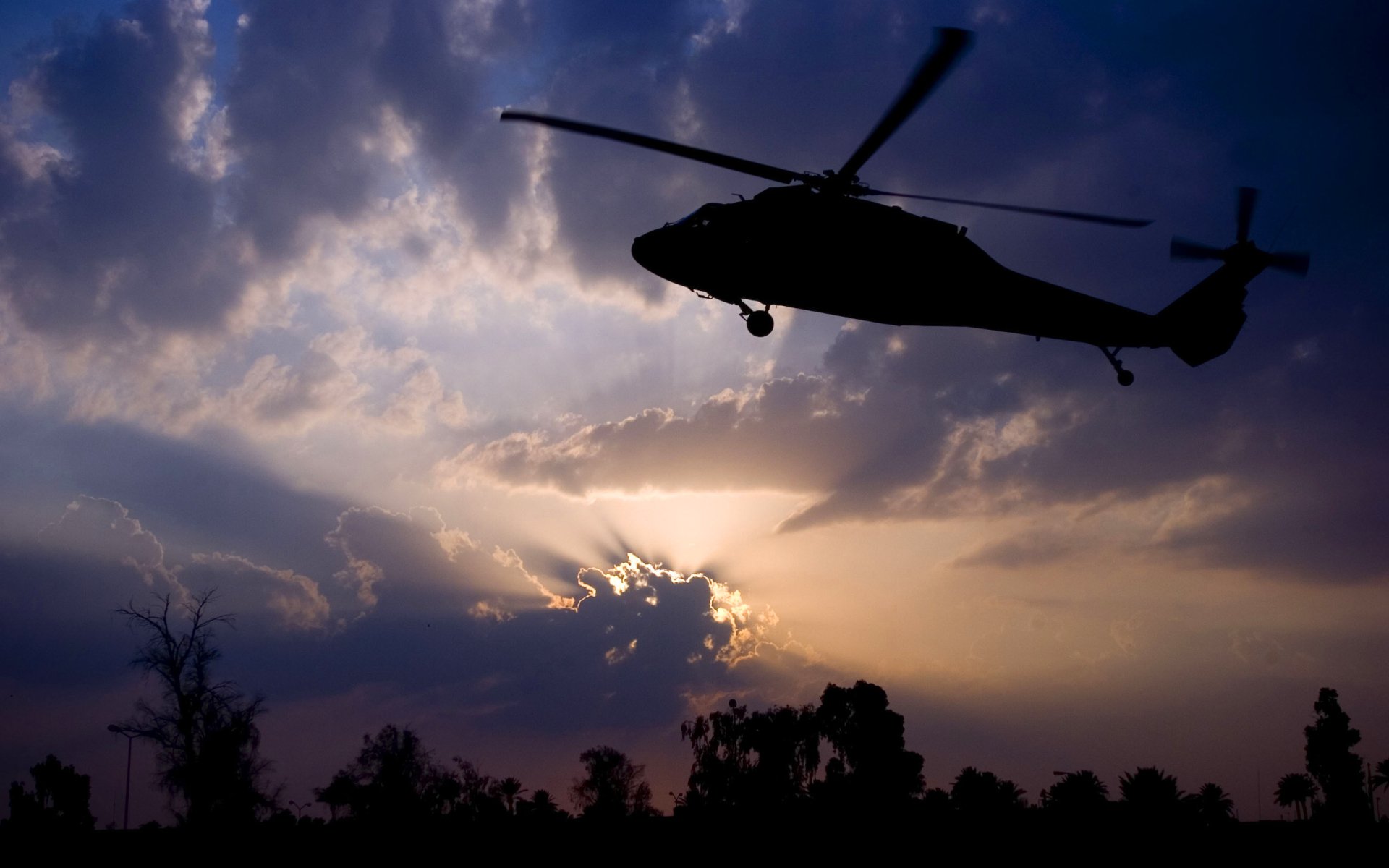 Silhouette of Sikorsky UH-60 Black Hawk military helicopter at dusk with sunburst clouds — 2K Quad HD PC desktop wallpaper background.