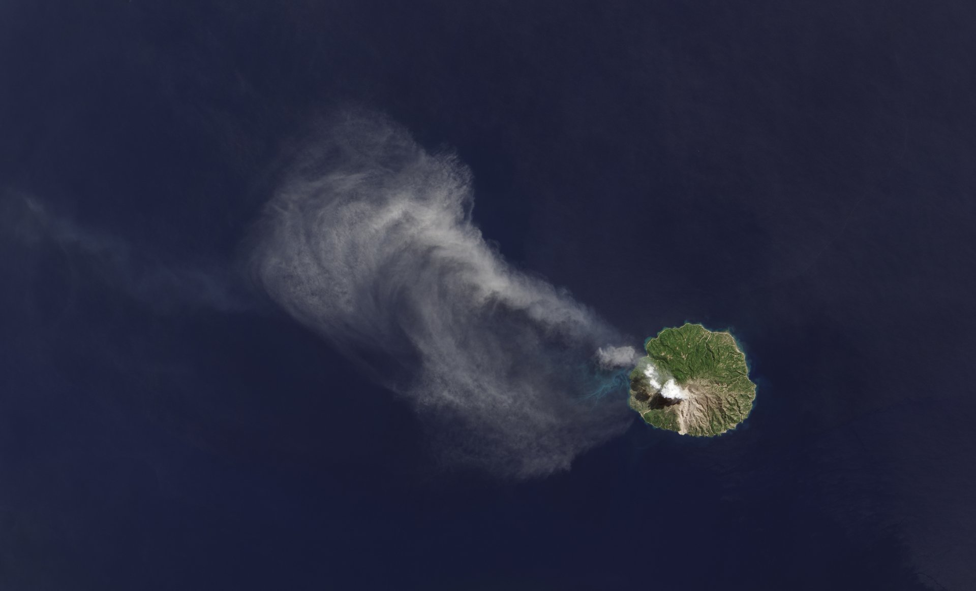 Nature, Earth From Space 4K Ultra HD PC desktop wallpaper and background showing a green volcanic island in the deep blue ocean emitting a long plume of smoke and vapor.