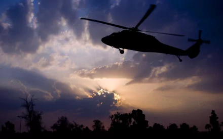 Silhouette of Sikorsky UH-60 Black Hawk military helicopter at dusk with sunburst clouds — 2K Quad HD PC desktop wallpaper background.