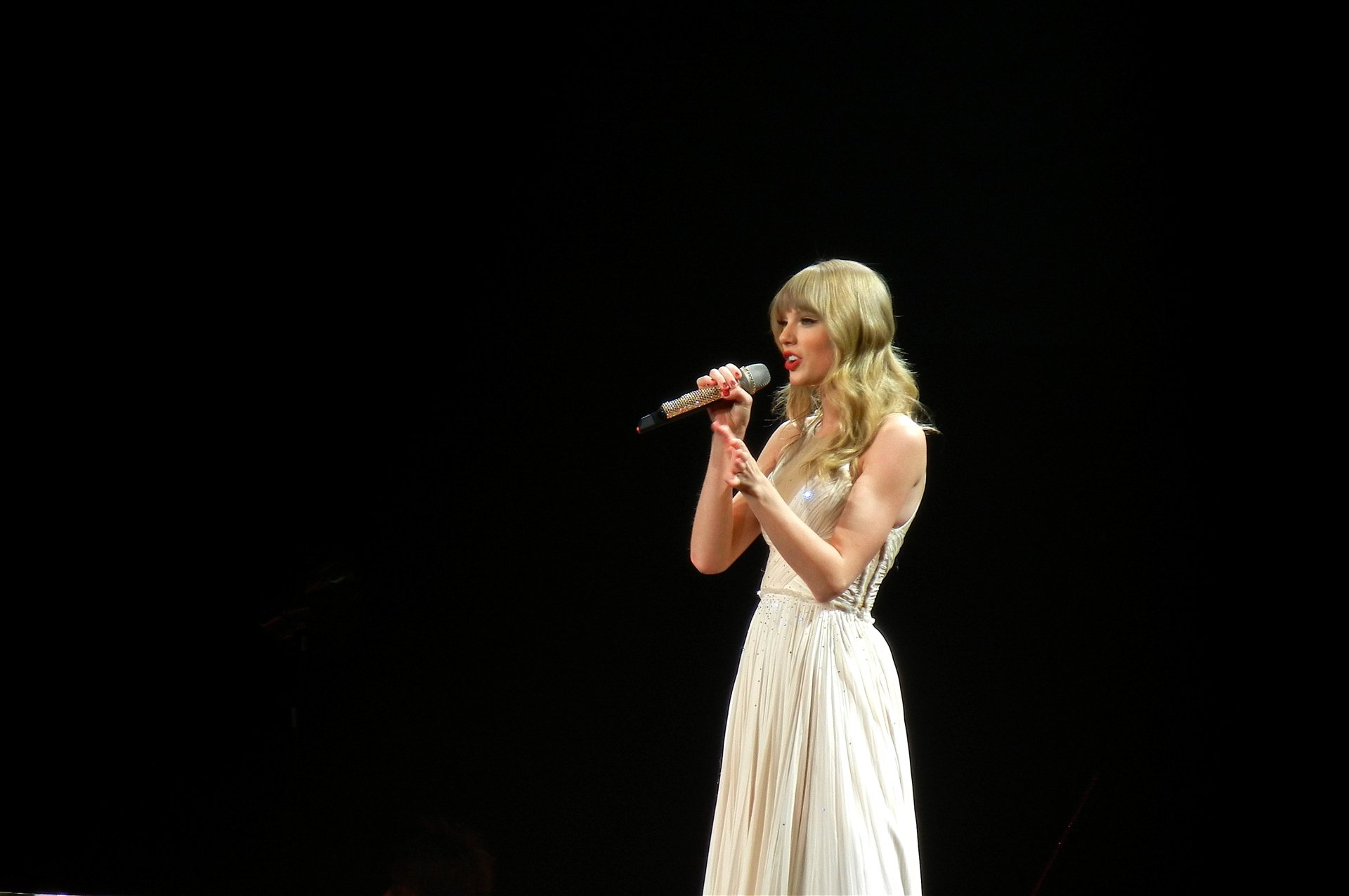 HD PC desktop wallpaper featuring Taylor Swift singing into a microphone on a dark stage, highlighting her music career.