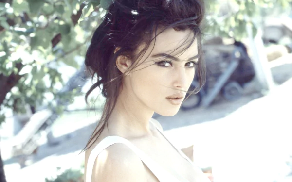 HD PC desktop wallpaper featuring celebrity Monica Bellucci posing outdoors with soft natural light filtering through leaves above.