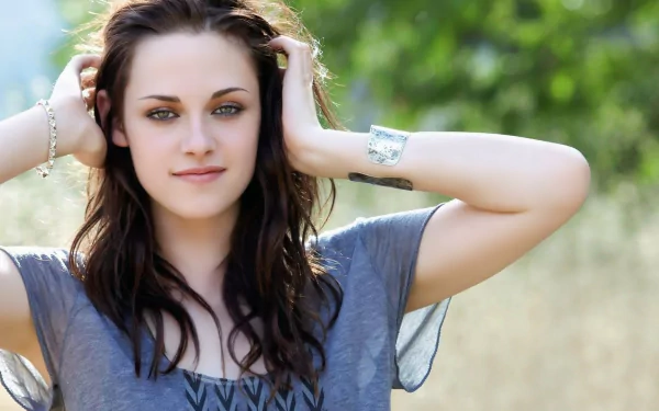 HD desktop wallpaper featuring a close-up image of Kristen Stewart outdoors, hands in hair, with a neutral expression and casual attire.