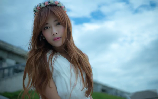 A Taiwanese model, Xiao Xi, poses with flowing brown hair and a floral crown against a backdrop of clouds, creating a serene and captivating image for a 4K Ultra HD wallpaper.