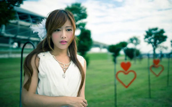 An HD wallpaper of a Taiwanese woman named Xiao Xi. The mood is serene, with the woman dressed in white, standing outdoors against a green lawn and heart-shaped decorations in the background.