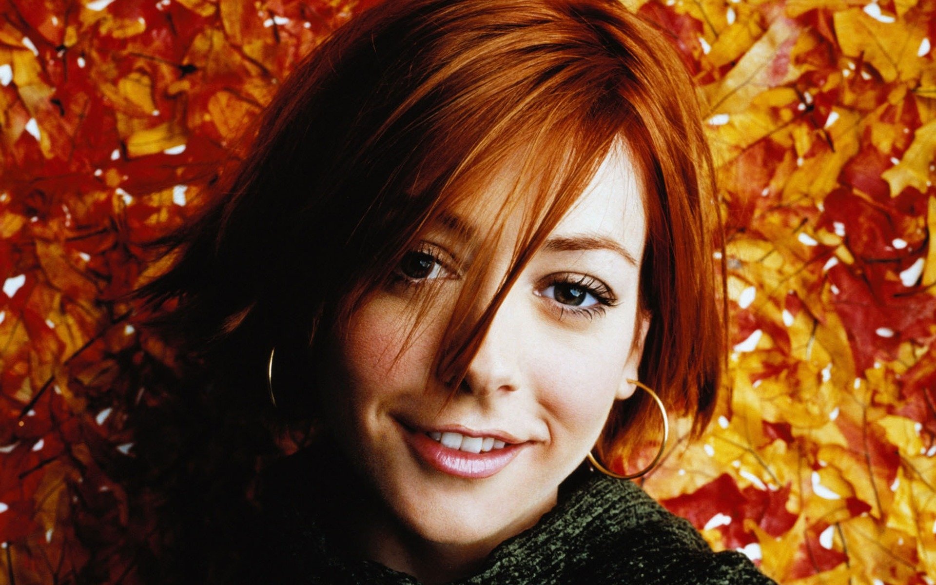 HD desktop wallpaper featuring celebrity Alyson Hannigan smiling against a vibrant orange autumn leaf background.