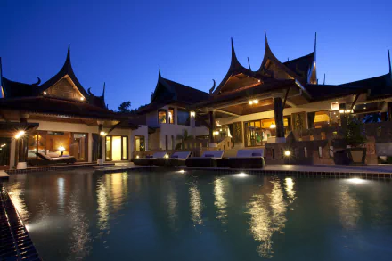 4K Ultra HD view of Danau Daun villa in Thailand, featuring traditional architecture with pointed roofs and a tranquil man-made pool at dusk.