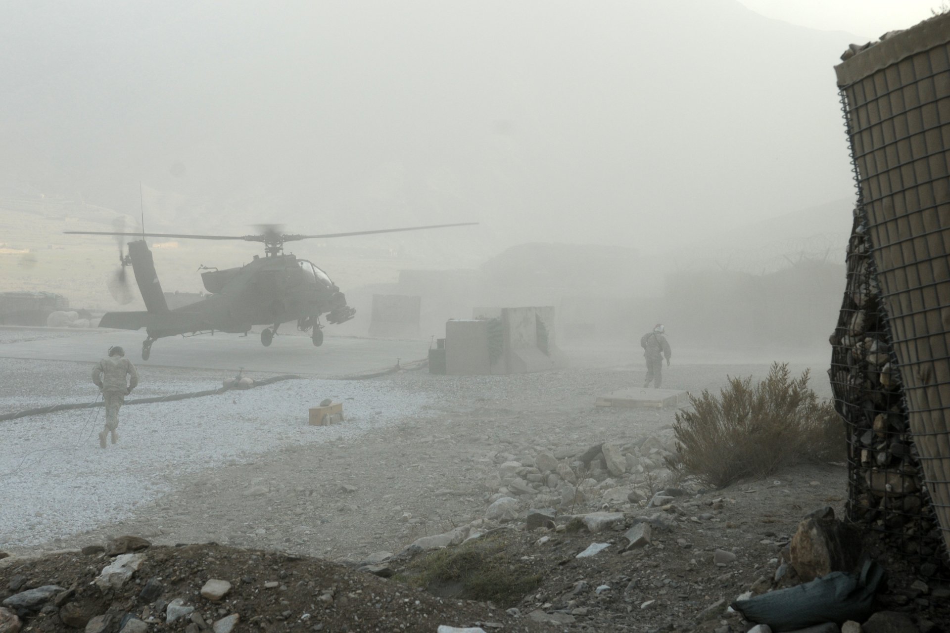 2K Quad HD PC desktop wallpaper of a Boeing AH-64 Apache kicking up dust over a military landing zone with soldiers nearby.