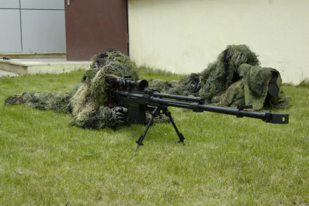 HD PC desktop wallpaper showing two military snipers camouflaged in ghillie suits lying prone on grass beside a building.