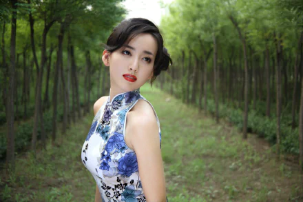A poised Chinese woman named Hú Yǐng Yí stands gracefully in a lush green forest, wearing a floral dress, captured in a stunning HD wallpaper background.